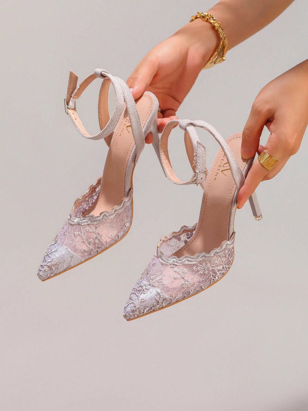 Lace embroidered high heels with thin stiletto heel, pointed toe, rhinestone embellishments, and ankle strap buckle closure.