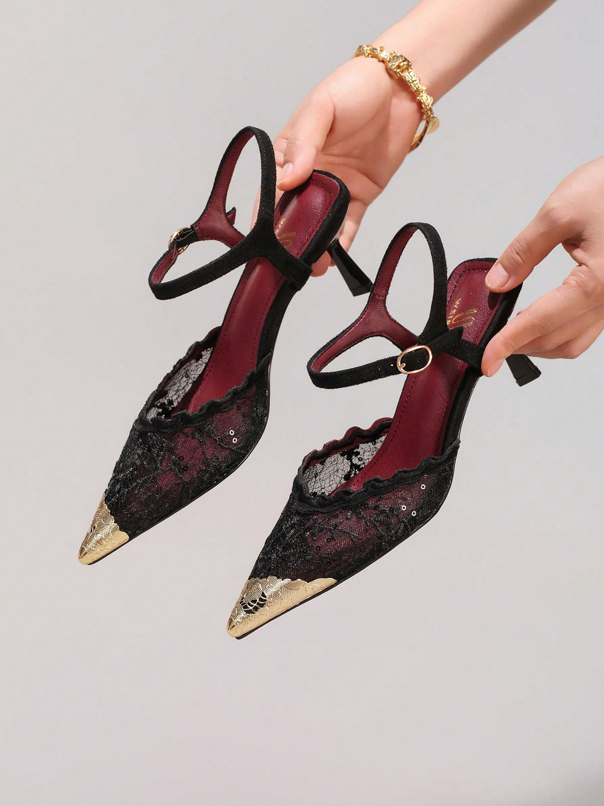 Lace embroidered high heels with thin stiletto heel, pointed toe, rhinestone embellishments, and ankle strap buckle closure.