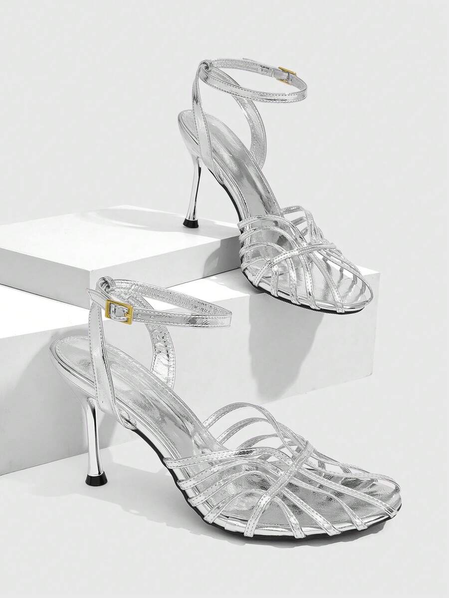 Women's glossy silver open-toed sandals with thin pyramid heel and strappy ribbon details.