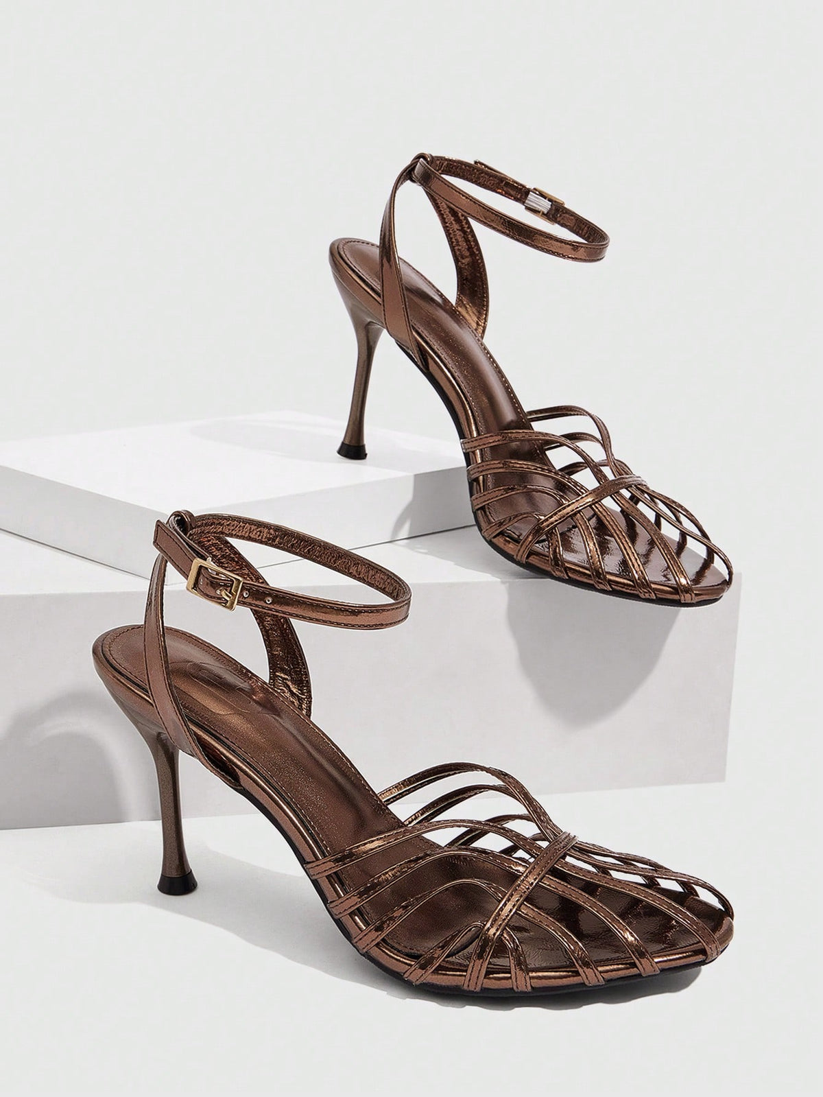 Women's glossy silver open-toed sandals with thin pyramid heel and strappy ribbon details.