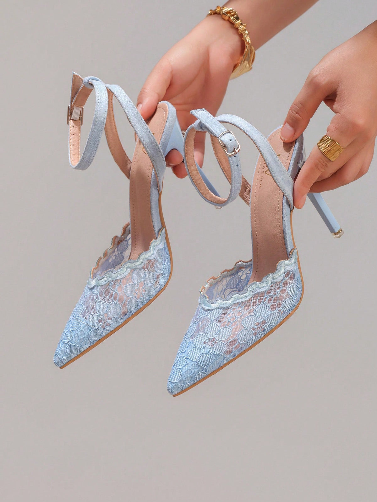 Lace embroidered high heels with thin stiletto heel, pointed toe, rhinestone embellishments, and ankle strap buckle closure.