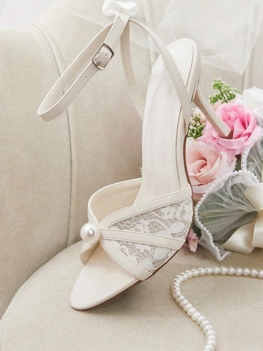 Beige high heel sandals with delicate lace overlay, pearl embellishments, stiletto heel, and adjustable ankle strap for bride and wedding party wear.