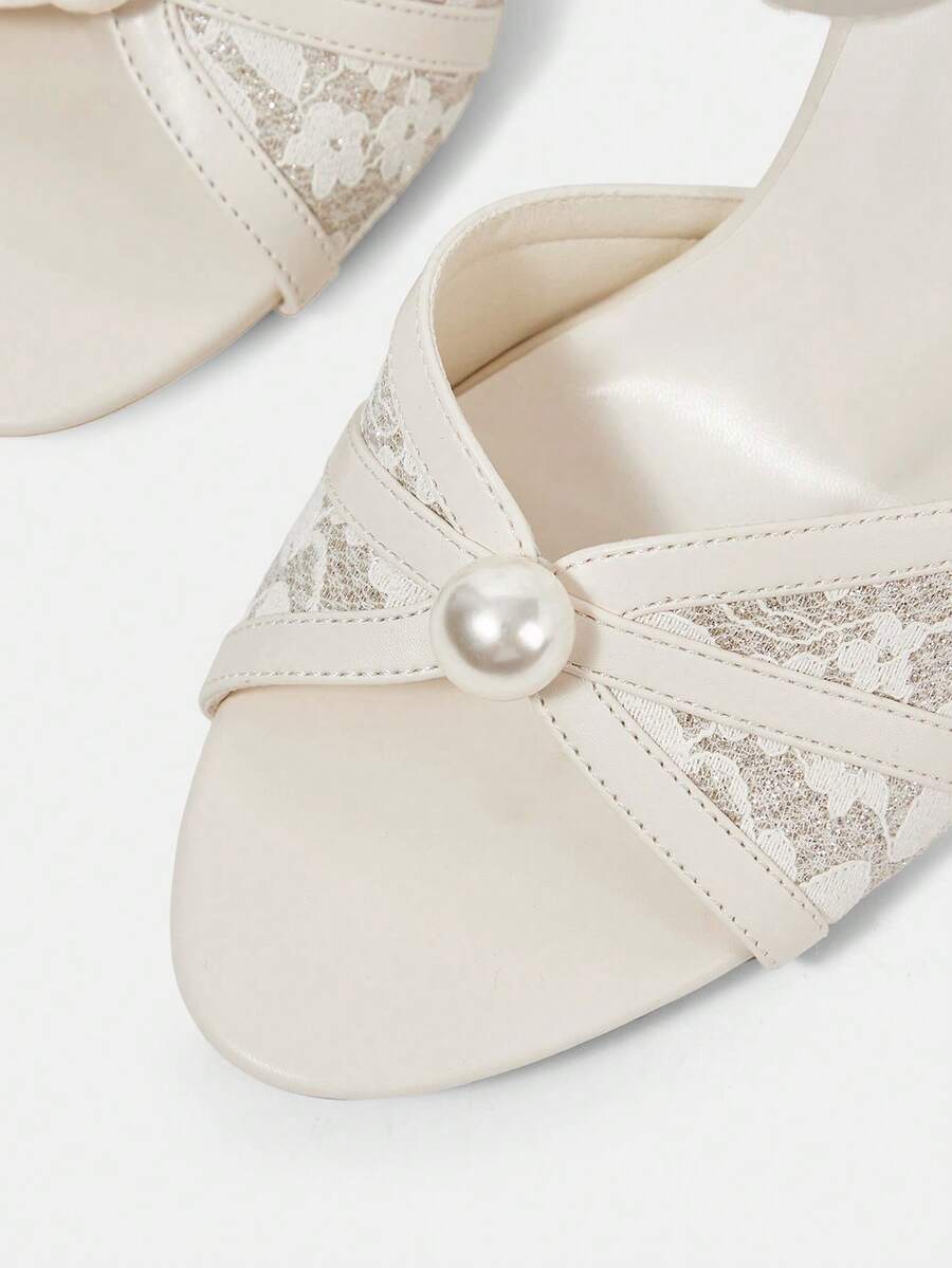 Beige high heel sandals with delicate lace overlay, pearl embellishments, stiletto heel, and adjustable ankle strap for bride and wedding party wear.