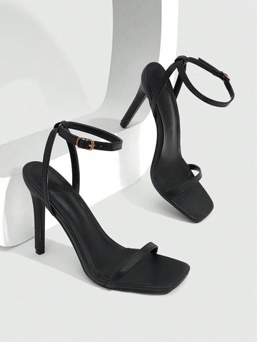 Women's minimalist black heeled sandals featuring an open toe, stiletto high heel, and adjustable ankle strap buckle closure.