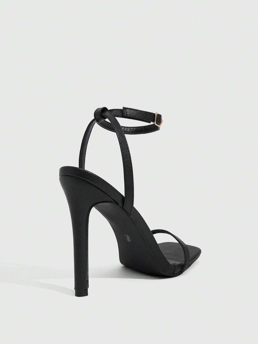 Women's minimalist black heeled sandals featuring an open toe, stiletto high heel, and adjustable ankle strap buckle closure.