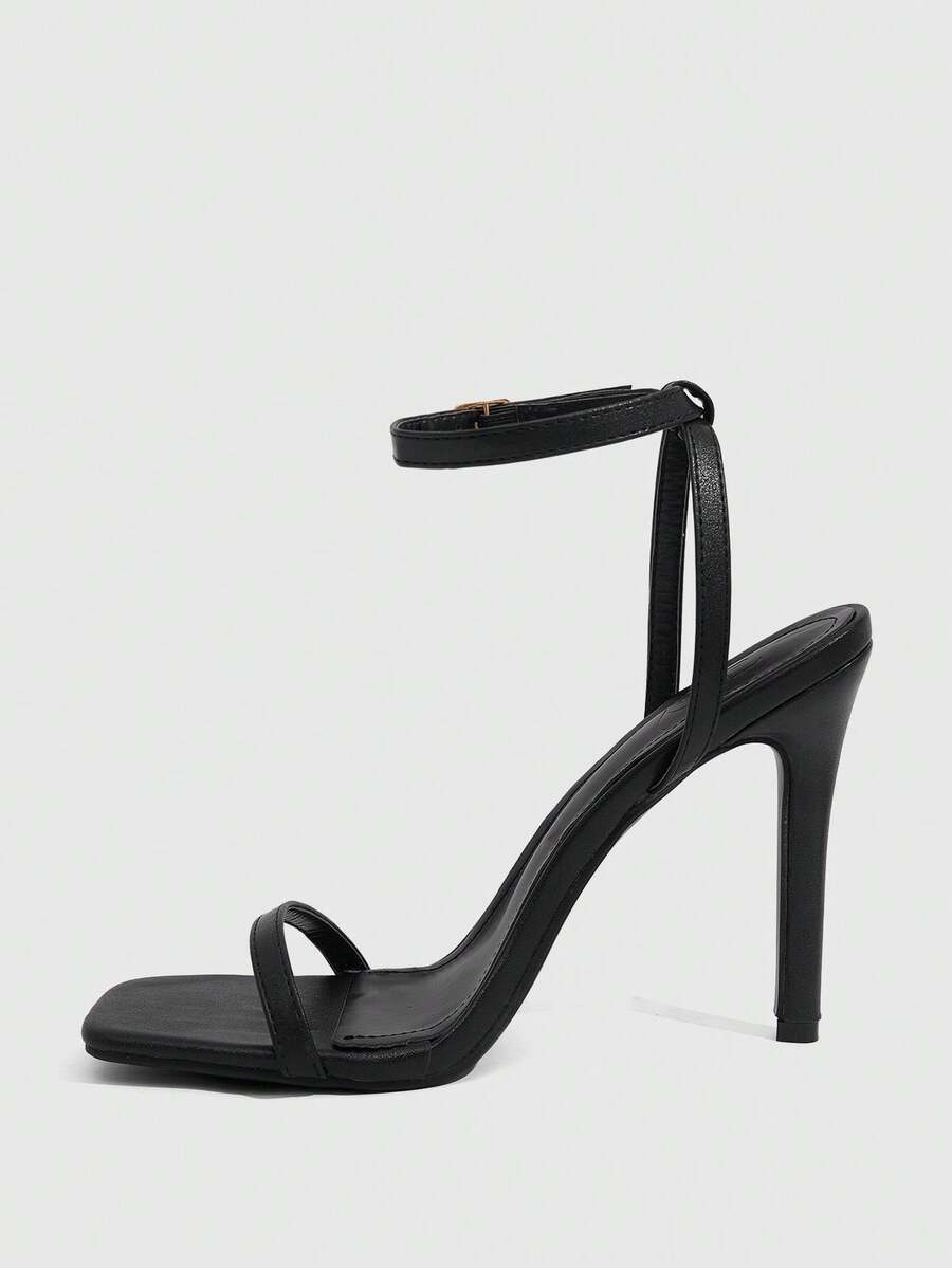 Women's minimalist black heeled sandals featuring an open toe, stiletto high heel, and adjustable ankle strap buckle closure.