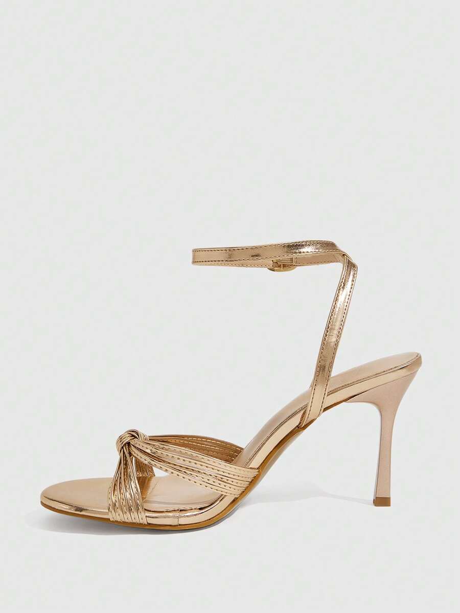 Women's champagne stiletto high heel sandals featuring knotted cross-over straps, open round toe, and adjustable ankle buckle strap.