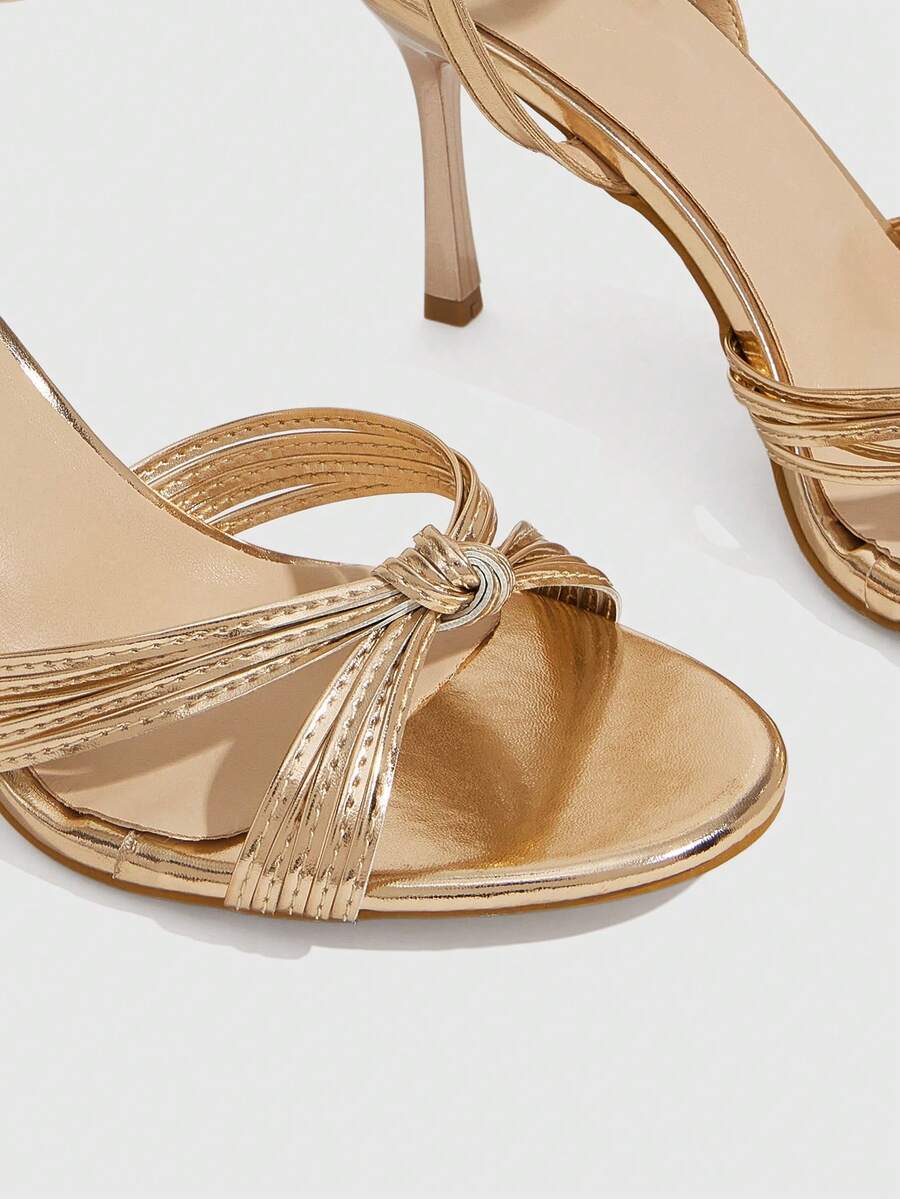 Women's champagne stiletto high heel sandals featuring knotted cross-over straps, open round toe, and adjustable ankle buckle strap.