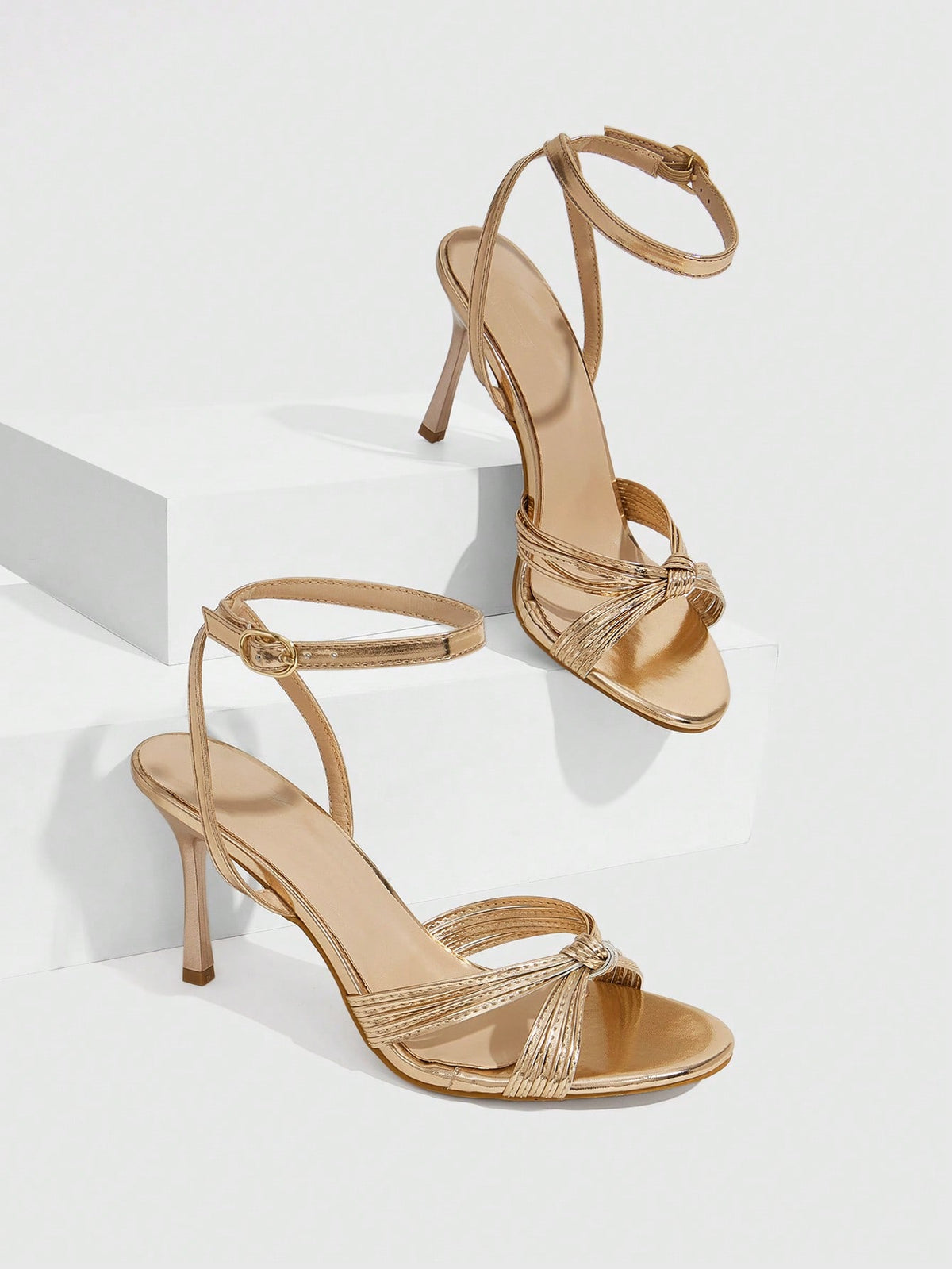 Women's champagne stiletto high heel sandals featuring knotted cross-over straps, open round toe, and adjustable ankle buckle strap.