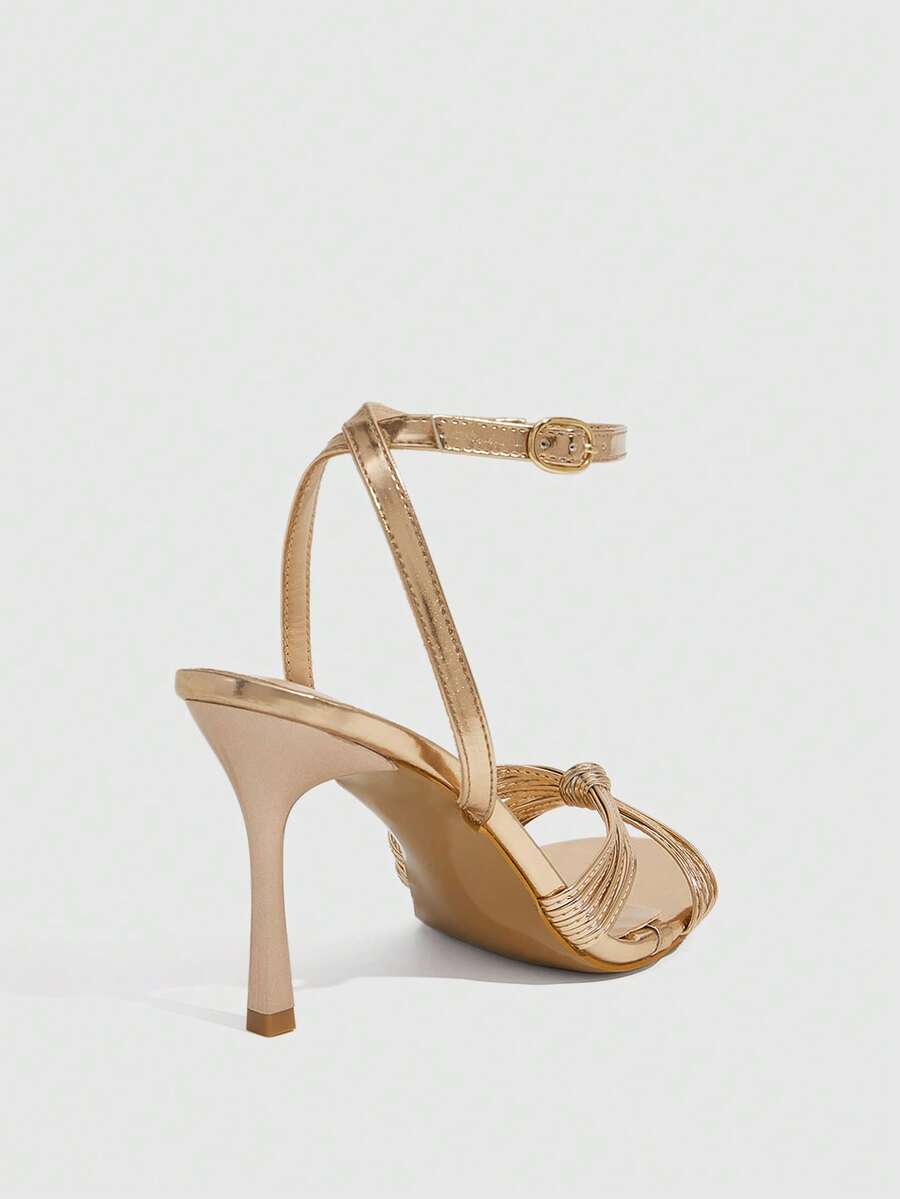 Women's champagne stiletto high heel sandals featuring knotted cross-over straps, open round toe, and adjustable ankle buckle strap.
