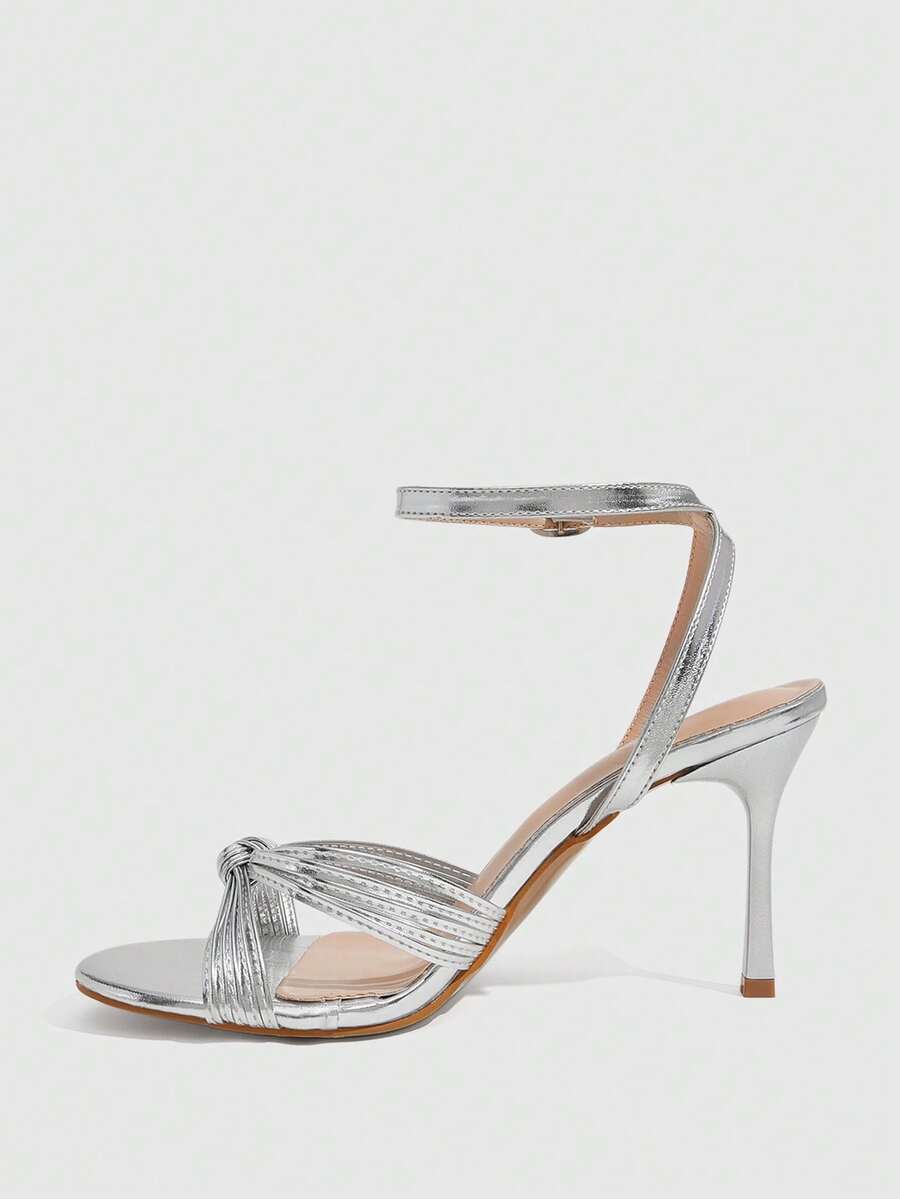 Women's champagne stiletto high heel sandals featuring knotted cross-over straps, open round toe, and adjustable ankle buckle strap.