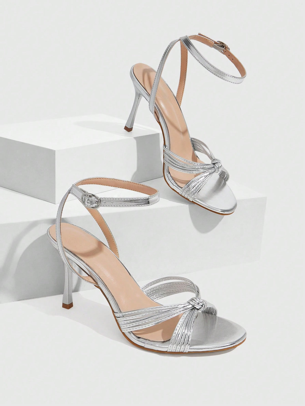 Women's champagne stiletto high heel sandals featuring knotted cross-over straps, open round toe, and adjustable ankle buckle strap.