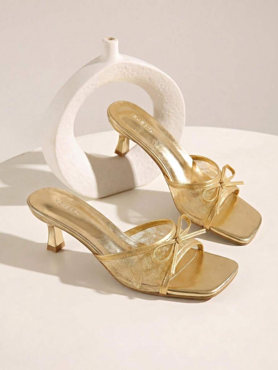 Gold kitten heel mule sandals featuring lace mesh bow detail and an open-toe slip-on design for women.