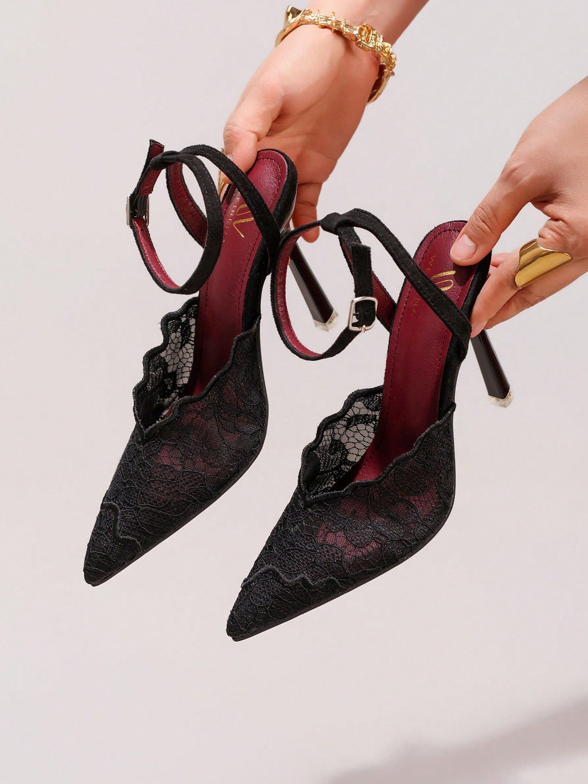 Lace embroidered high heels with thin stiletto heel, pointed toe, rhinestone embellishments, and ankle strap buckle closure.