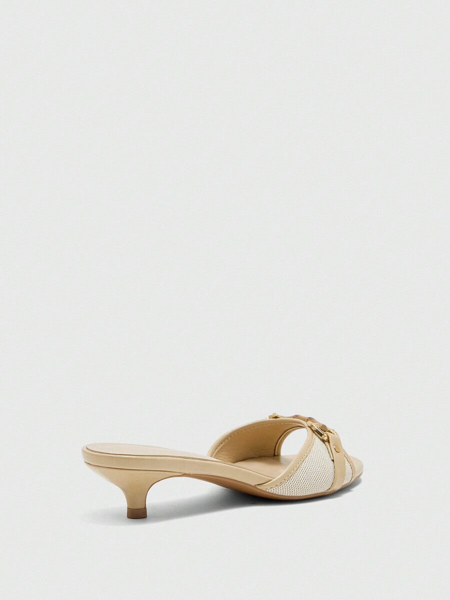 Beige women's slip-on kitten heel slide sandals featuring an accent buckle with grommet eyelets.