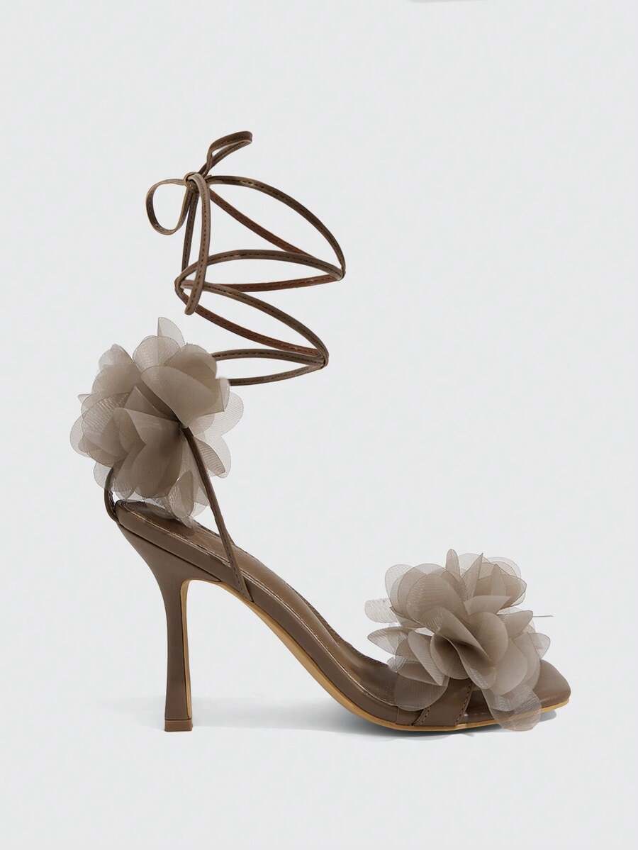 Women's open toe heeled sandals featuring 3D floral decor, satin lace-up ankle straps, and stiletto high heels.