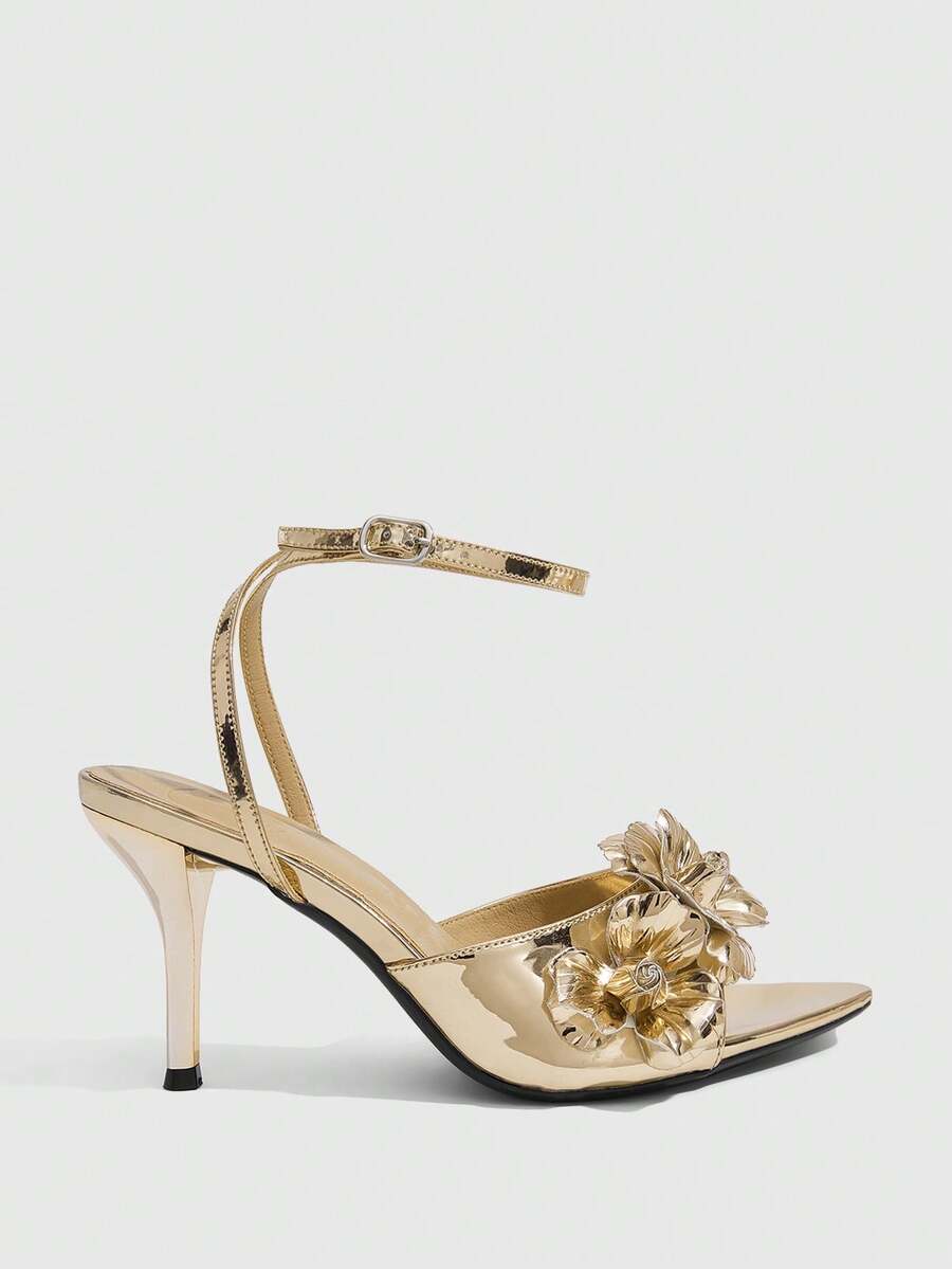Champagne stiletto high heel sandals featuring a flower detail, open toe, and buckle back strap.
