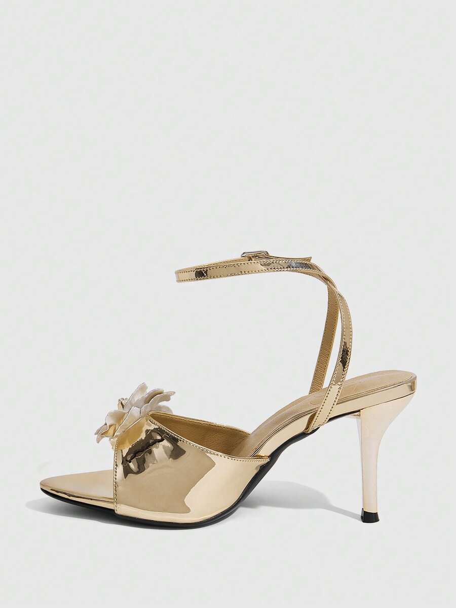 Champagne stiletto high heel sandals featuring a flower detail, open toe, and buckle back strap.