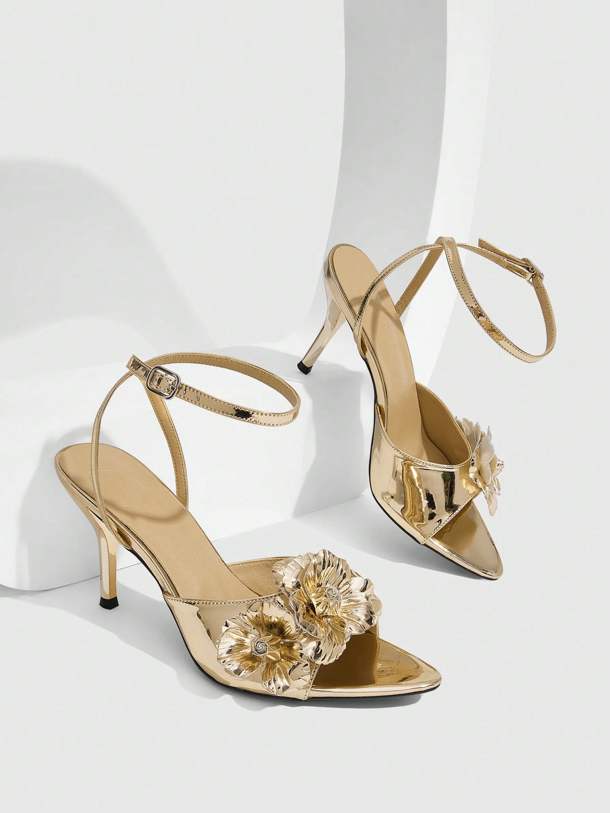 Champagne stiletto high heel sandals featuring a flower detail, open toe, and buckle back strap.