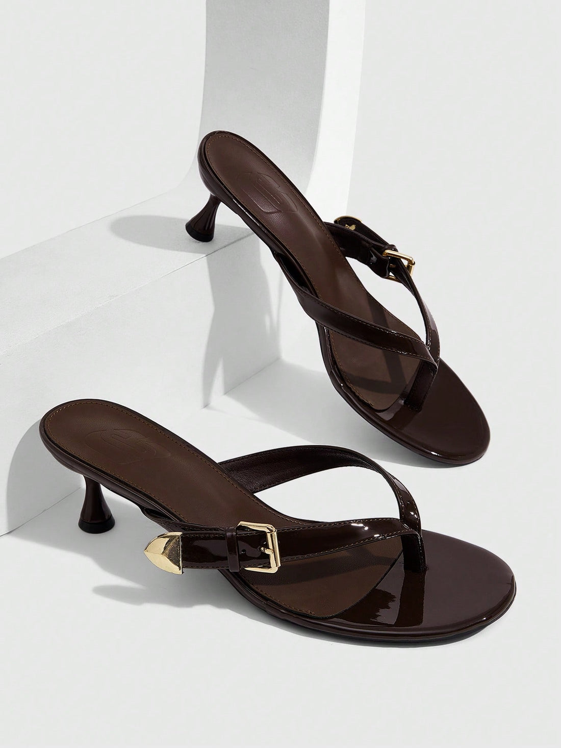 Women's patent leather heeled sandals featuring a toe post strap with metal buckle and mid pyramid heel.