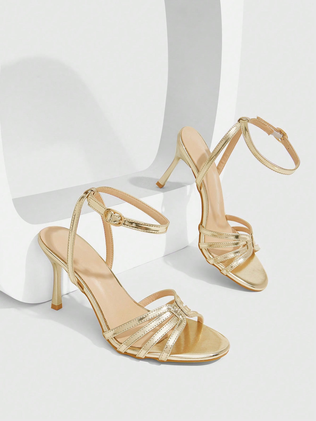 Women's champagne stiletto high heel sandals featuring knotted cross-over straps, open round toe, and adjustable ankle buckle strap.