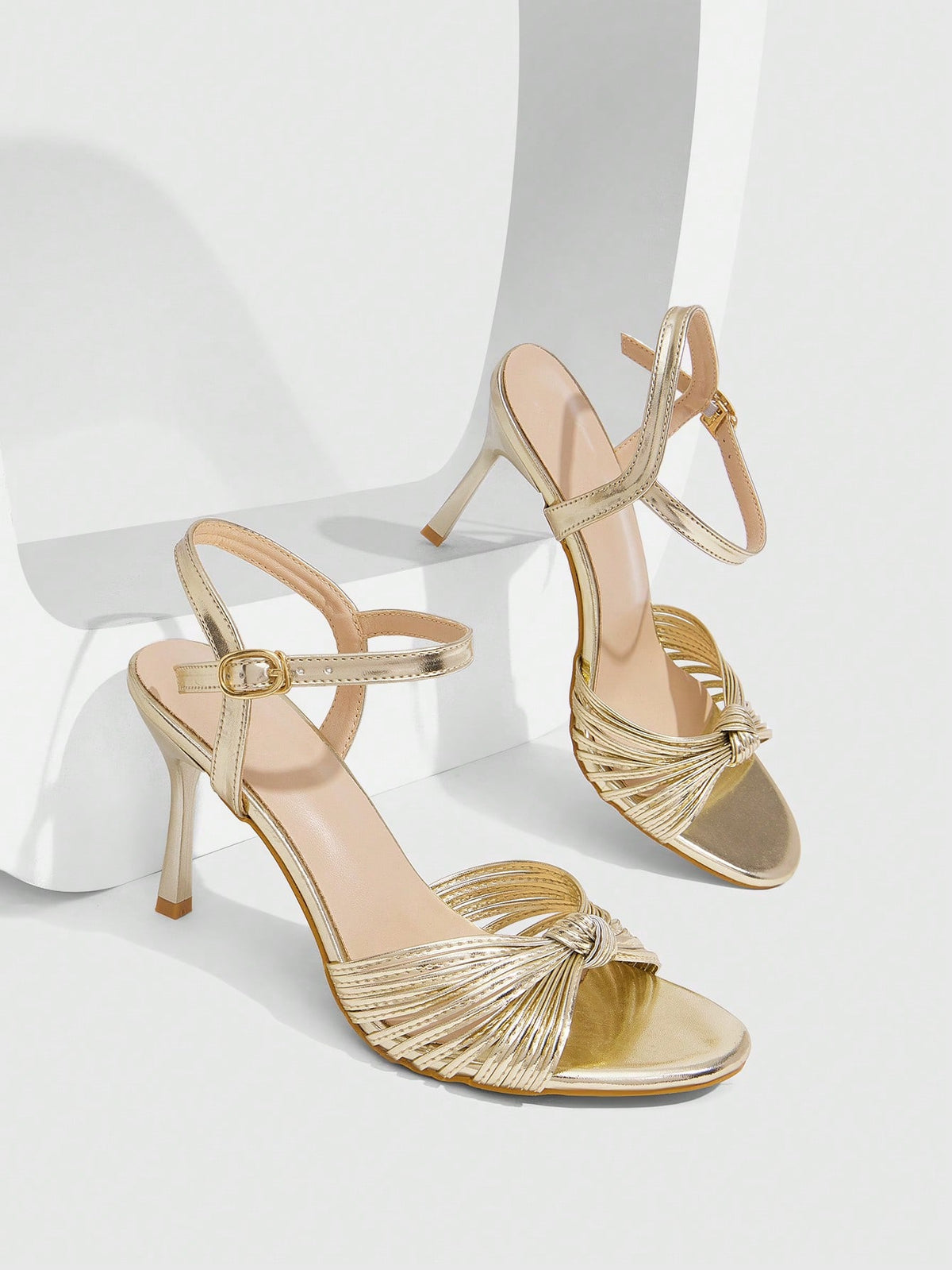 Women's champagne stiletto high heel sandals featuring knotted cross-over straps, open round toe, and adjustable ankle buckle strap.