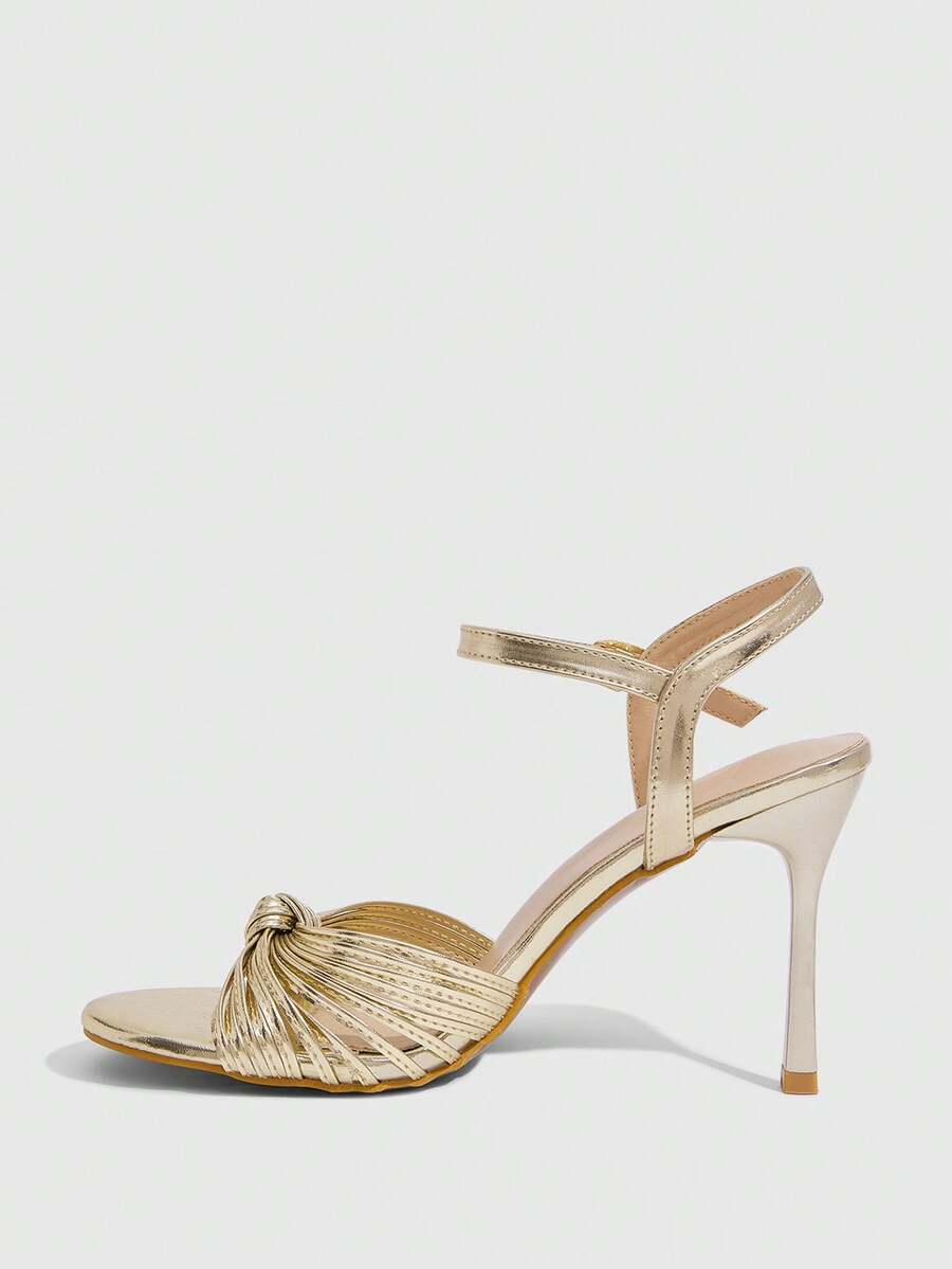Women's champagne stiletto high heel sandals featuring knotted cross-over straps, open round toe, and adjustable ankle buckle strap.