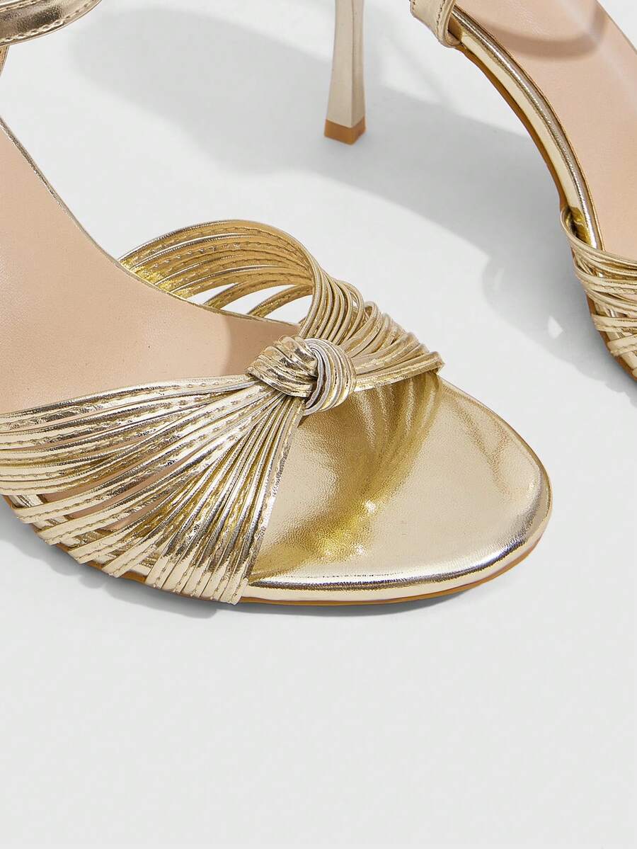 Women's champagne stiletto high heel sandals featuring knotted cross-over straps, open round toe, and adjustable ankle buckle strap.