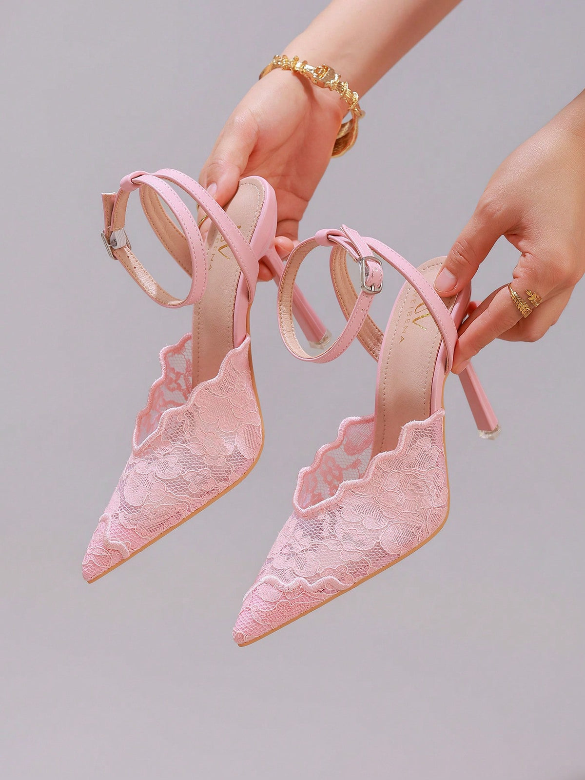 Lace embroidered high heels with thin stiletto heel, pointed toe, rhinestone embellishments, and ankle strap buckle closure.