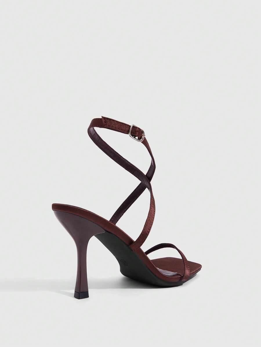 Pair of women's brown satin open toe stiletto sandals with cross ankle buckle straps.