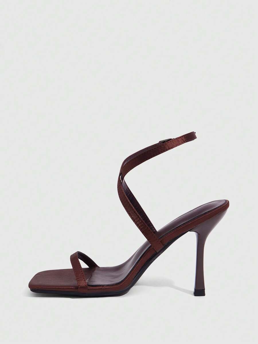 Pair of women's brown satin open toe stiletto sandals with cross ankle buckle straps.