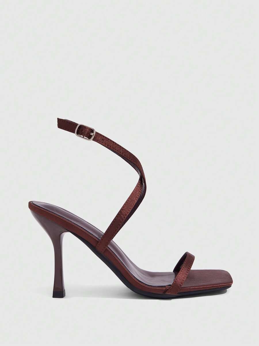 Pair of women's brown satin open toe stiletto sandals with cross ankle buckle straps.