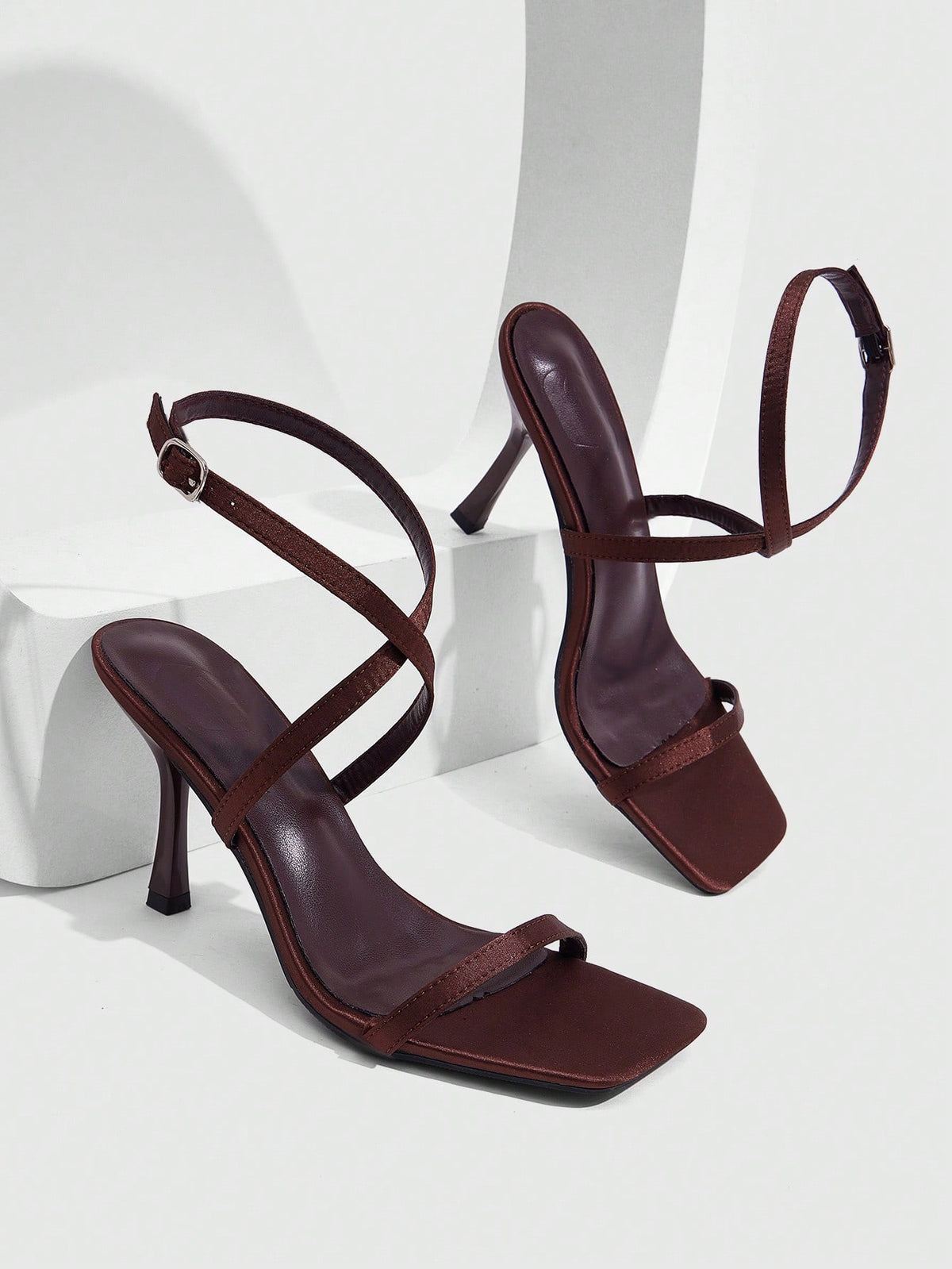Pair of women's brown satin open toe stiletto sandals with cross ankle buckle straps.