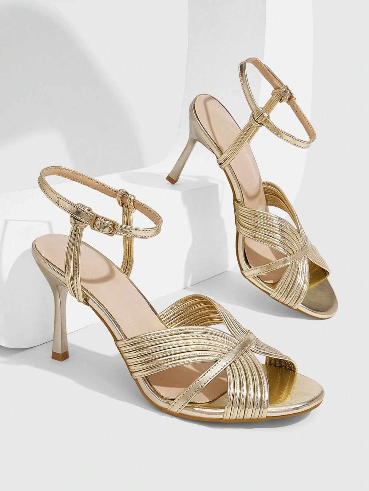 Women's champagne stiletto high heel sandals featuring knotted cross-over straps, open round toe, and adjustable ankle buckle strap.