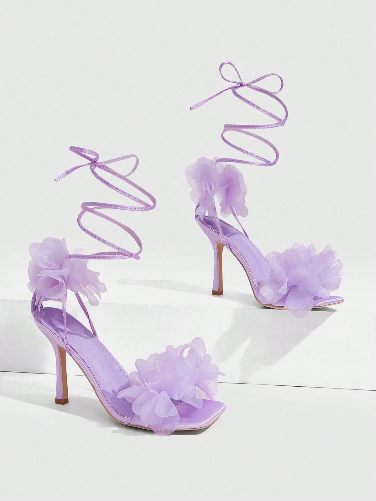 Women's open toe heeled sandals featuring 3D floral decor, satin lace-up ankle straps, and stiletto high heels.
