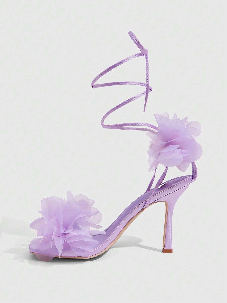Women's open toe heeled sandals featuring 3D floral decor, satin lace-up ankle straps, and stiletto high heels.