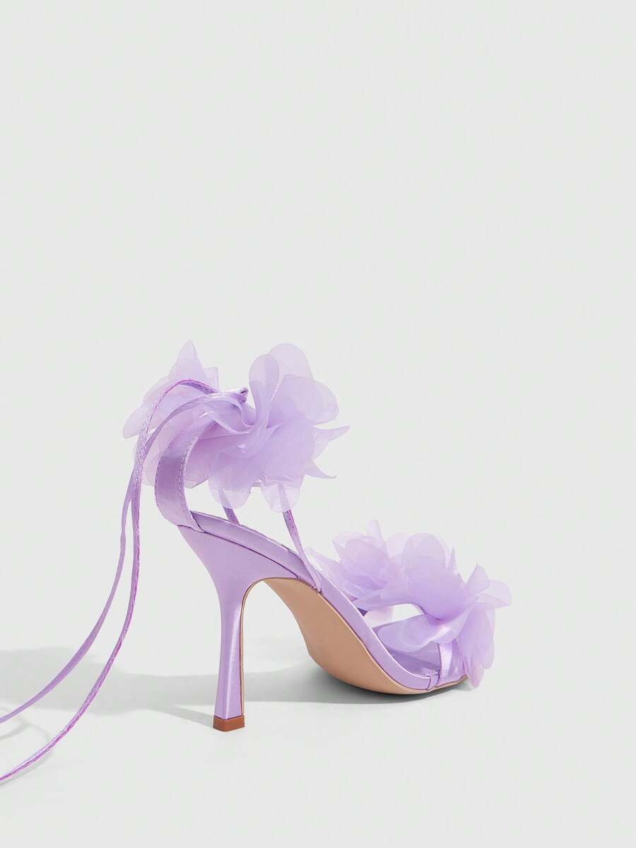 Women's open toe heeled sandals featuring 3D floral decor, satin lace-up ankle straps, and stiletto high heels.