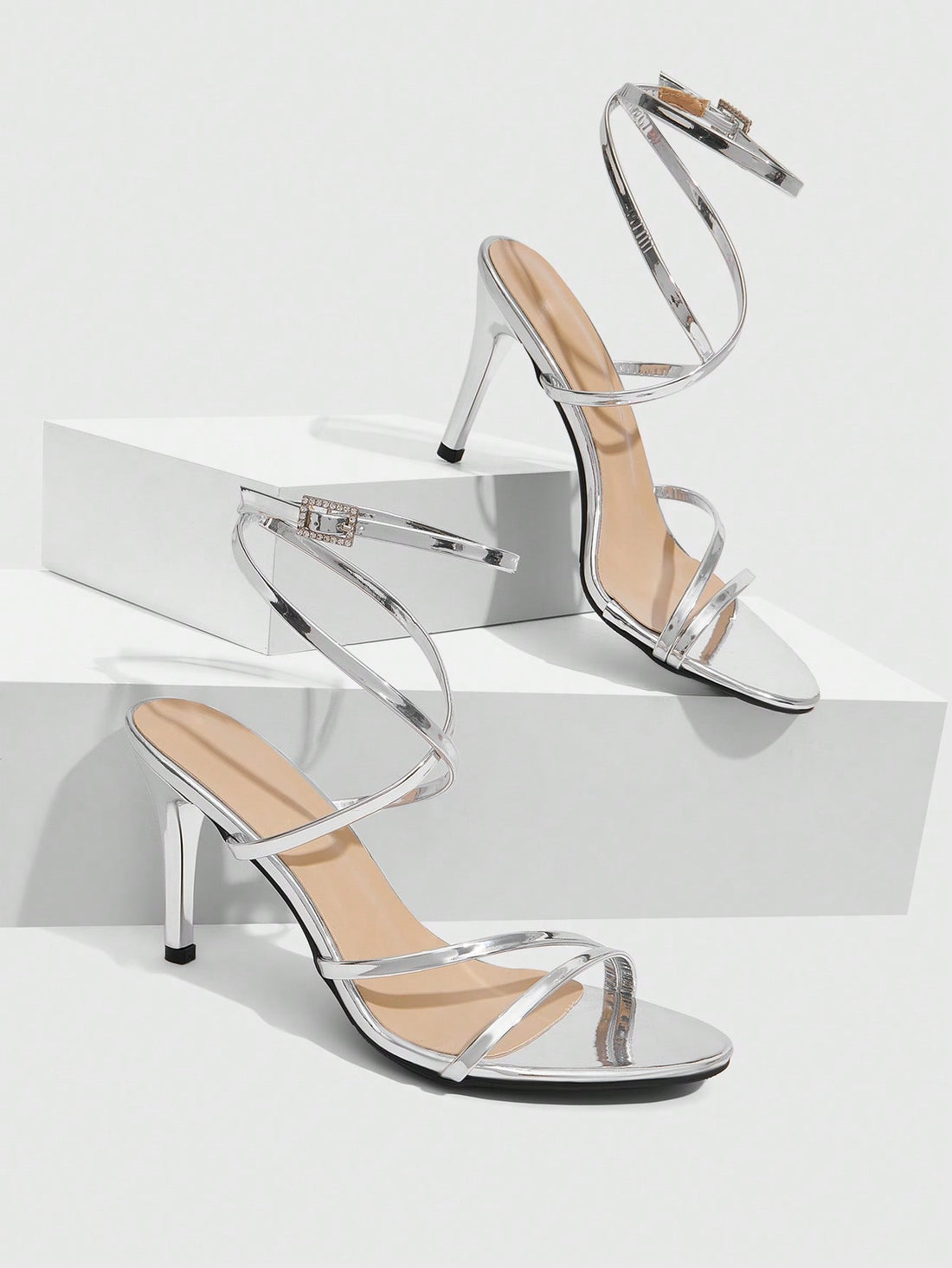 Silver high-heeled sandals featuring a rhinestone buckle ankle strap and sleek stiletto heel.
