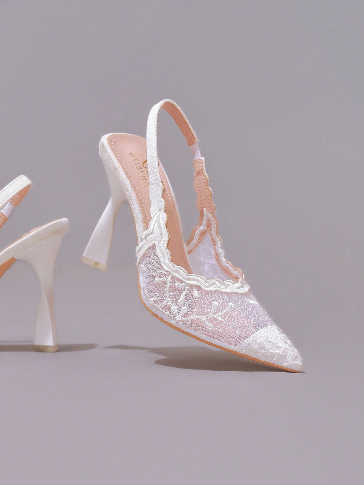 Lace embroidered high heels with thin stiletto heel, pointed toe, rhinestone embellishments, and ankle strap buckle closure.