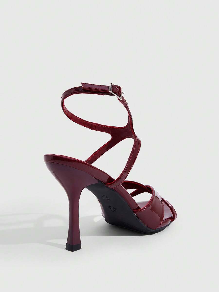 Women's glossy patent leather stiletto sandals in burgundy with open toe design and buckle strap closure.
