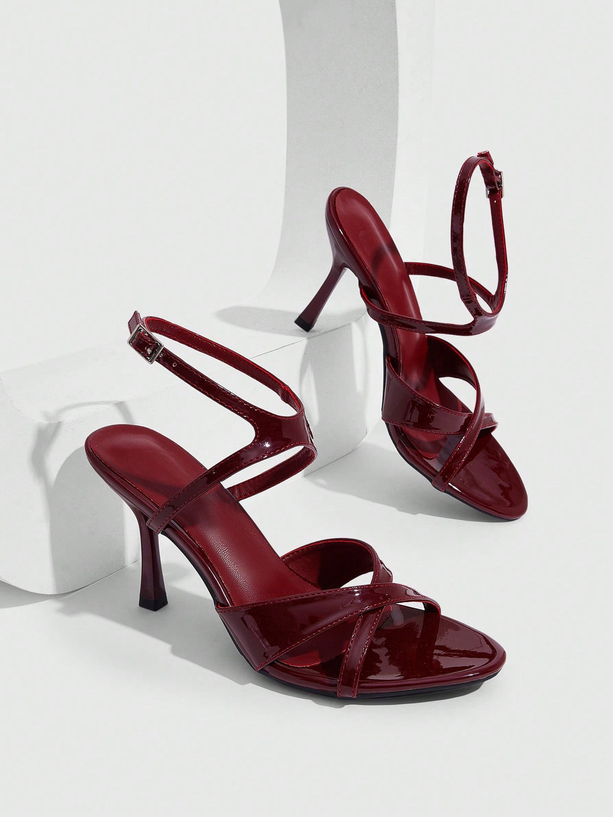 Women's glossy patent leather stiletto sandals in burgundy with open toe design and buckle strap closure.