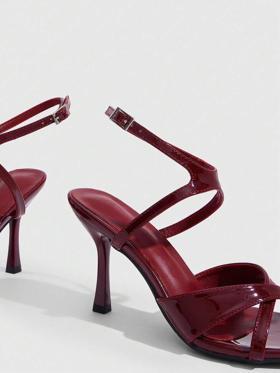 Women's glossy patent leather stiletto sandals in burgundy with open toe design and buckle strap closure.