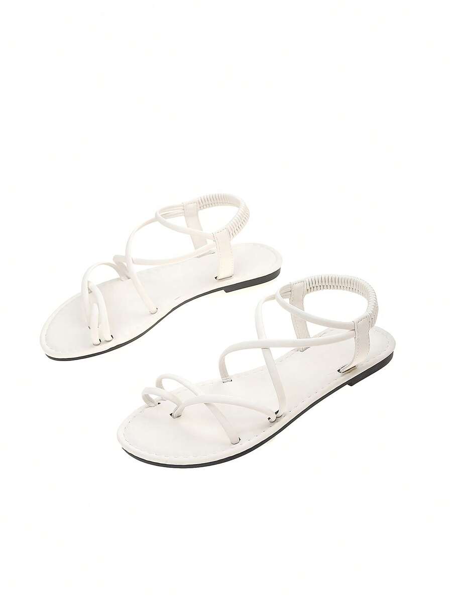 Flat sandals featuring thin criss-cross straps, elastic back strap, round toe post design, and smooth flat rubber sole.