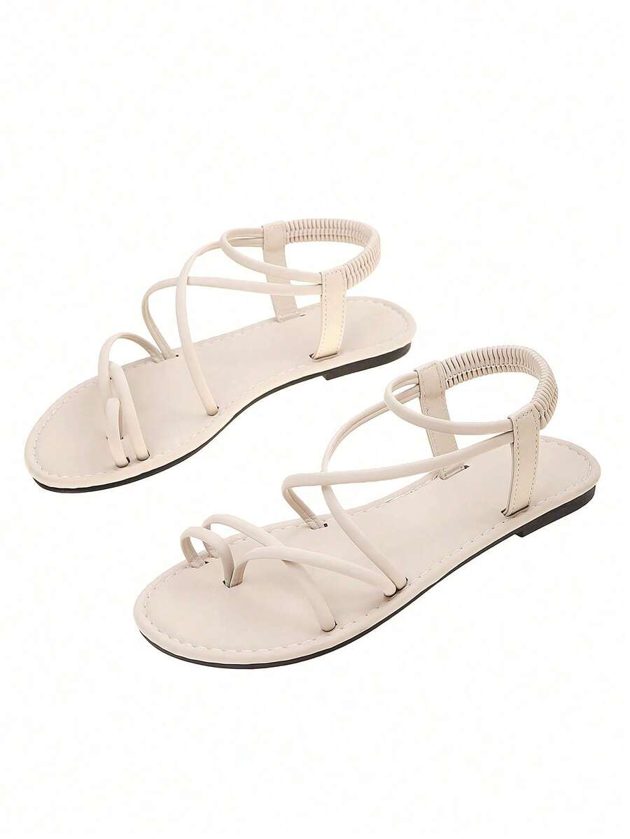 Flat sandals featuring thin criss-cross straps, elastic back strap, round toe post design, and smooth flat rubber sole.