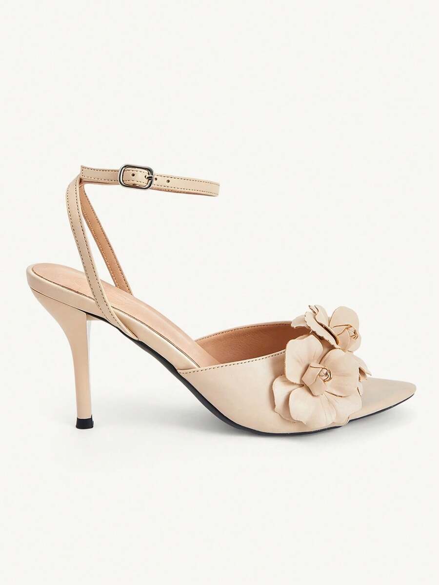 Champagne stiletto high heel sandals featuring a flower detail, open toe, and buckle back strap.