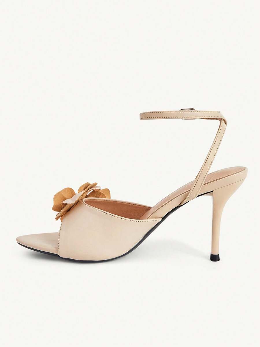 Champagne stiletto high heel sandals featuring a flower detail, open toe, and buckle back strap.