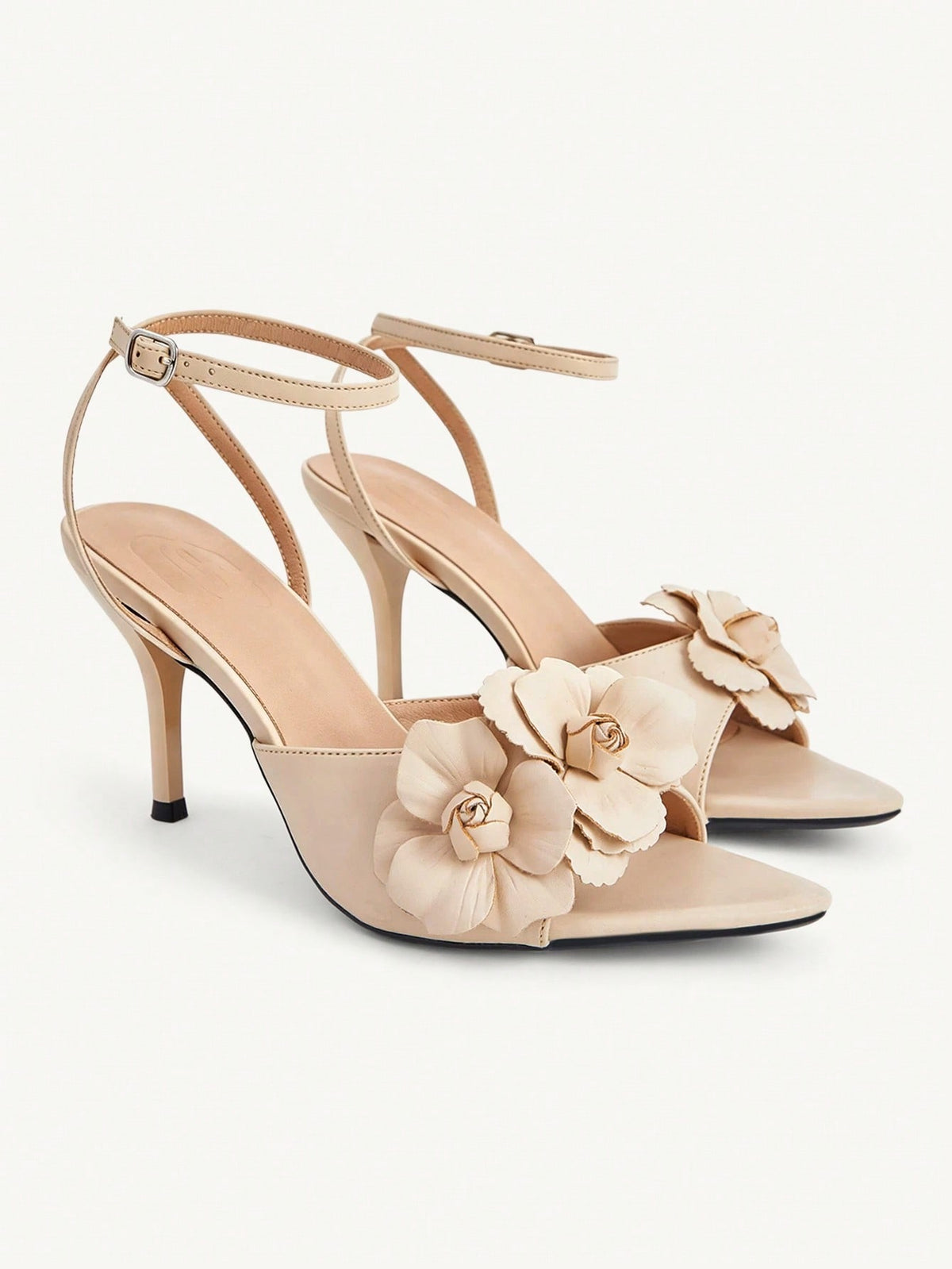 Champagne stiletto high heel sandals featuring a flower detail, open toe, and buckle back strap.