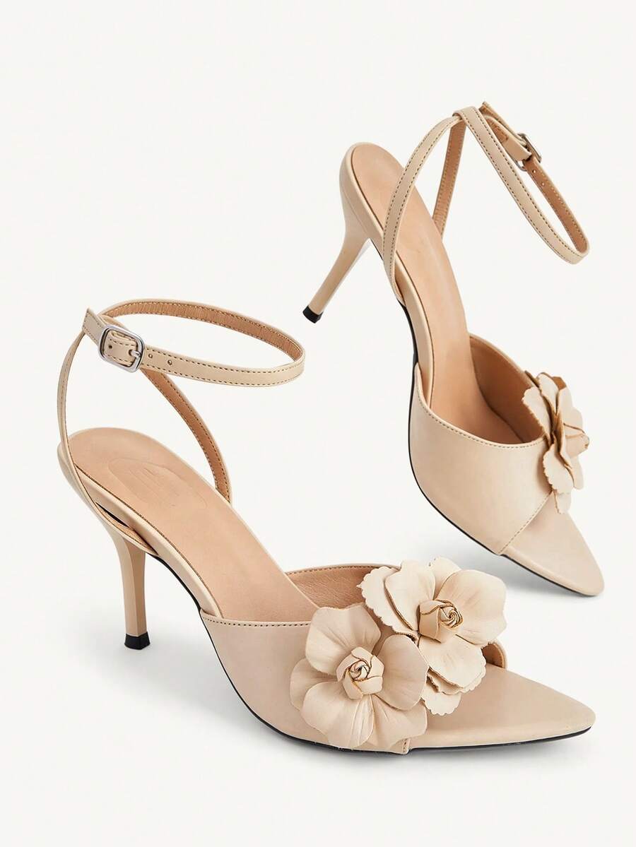 Champagne stiletto high heel sandals featuring a flower detail, open toe, and buckle back strap.