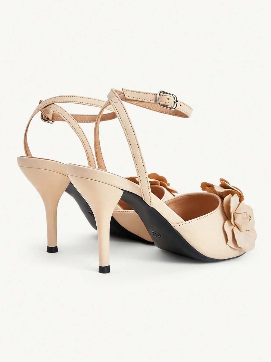 Champagne stiletto high heel sandals featuring a flower detail, open toe, and buckle back strap.