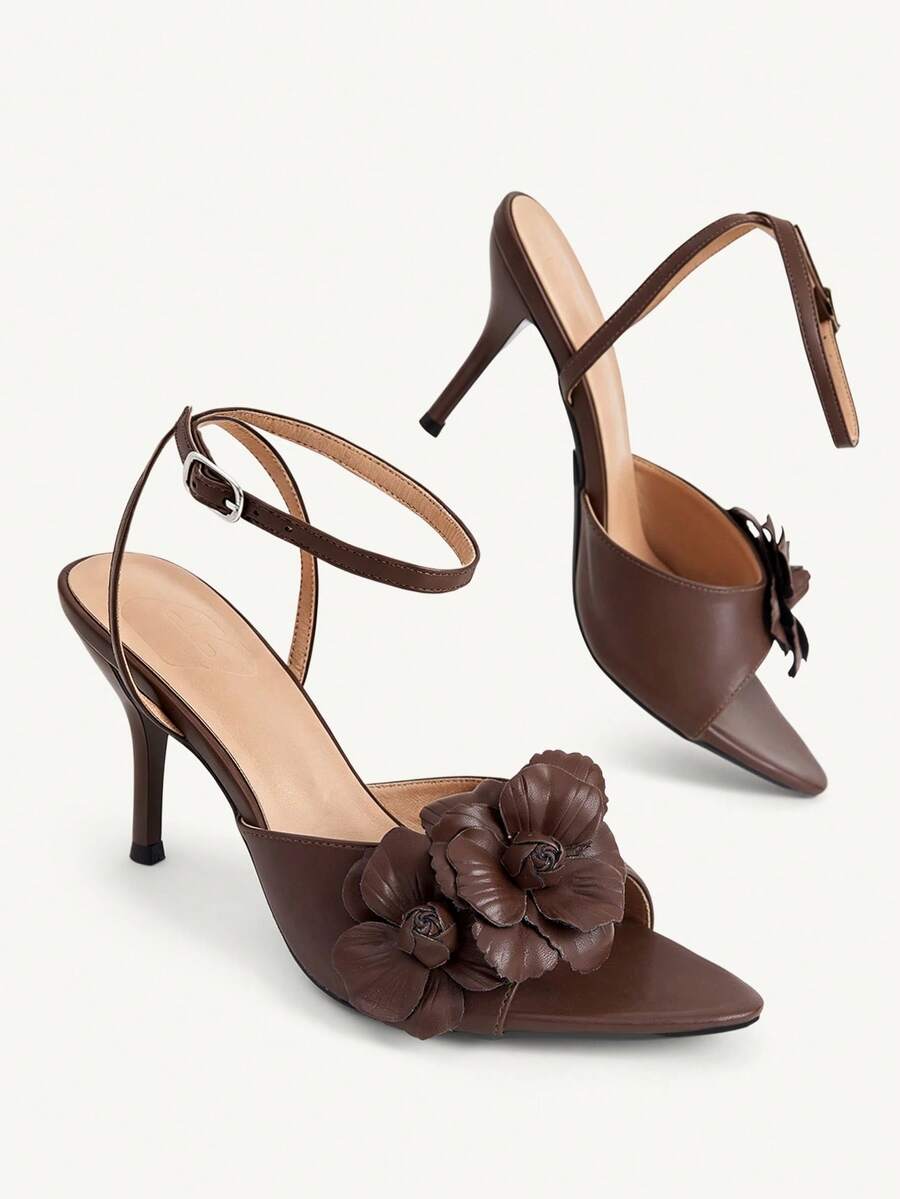 Champagne stiletto high heel sandals featuring a flower detail, open toe, and buckle back strap.